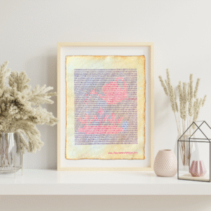 Handmade typewriter art on handmade, recycled, deckled-edged cotton paper. The repeated word “garden” is hand typed in black on a typewriter. The red text forms a visual of a watering can and small seedlings among the black text. The piece rests in a neutral frame on a white shelf styled with dried pampas grass, a glass terrarium, and pink textured vases to the sides. At the bottom of the art, the website “www.PlantsAreMyType.com” appears in red.