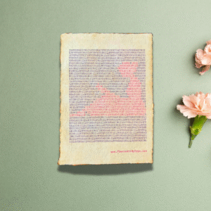 Handmade typewriter art on handmade, recycled, deckled-edged cotton paper. The repeated word “garden” is hand typed in black on a typewriter. The red text forms a visual of a watering can and small seedlings among the black text. The piece is displayed on a sage green background with light pink carnations arranged to the right. At the bottom of the art, the website “www.PlantsAreMyType.com” appears in red.