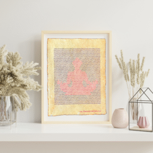 Handmade typewriter art on handmade, recycled, deckled-edged cotton paper. The repeated word “yoga” is hand typed in black on a typewriter. Red letters form a visual of a seated meditator among the black text. The piece rests in a neutral frame on a white shelf styled with dried pampas grass, a glass terrarium, and pink textured vases to the sides. At the bottom of the art, the website “www.PlantsAreMyType.com” appears in red.