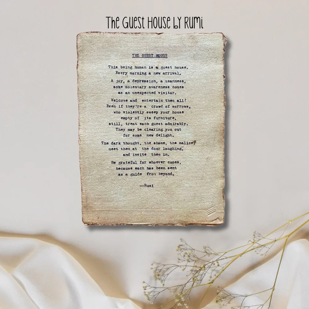 The guest house by Rumi poem hand typed on handmade, recycled cotton paper. The page is displayed atop a neutral, satin fabric background with a whispy dried flower at the bottom.