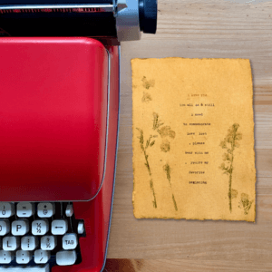 An image of a red typewriter next to typewriter art. The art is stamped with real flowers and displays a poem about love.