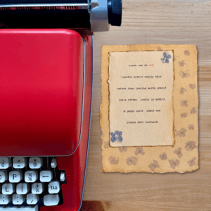 An image of a red typewriter next to typewriter art. The art is stamped with real flowers and displays a poem about love.