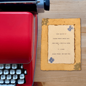 An image of a red typewriter next to typewriter art. The art is stamped with real flowers and displays a poem about love.