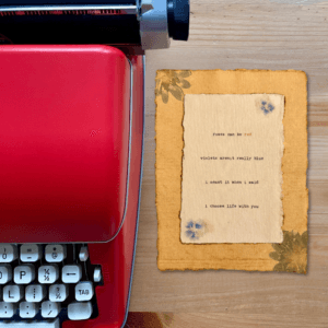 An image of a red typewriter next to typewriter art. The art is stamped with real flowers and displays a poem about love.