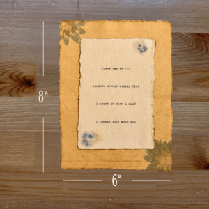 Typewriter art on a wooden background. There are guides showing the paper size, 6"x8". The page is stamped with real flowers and displays a poem about love.