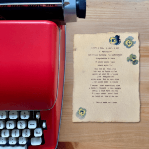 An image of a red typewriter next to typewriter art. The art is stamped with real flowers and displays a poem about love.
