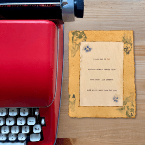 An image of a red typewriter next to typewriter art. The art is stamped with real flowers and displays a poem about love.