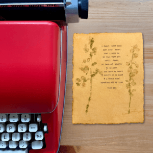 An image of a red typewriter next to typewriter art. The art is stamped with real flowers and displays a poem about love.